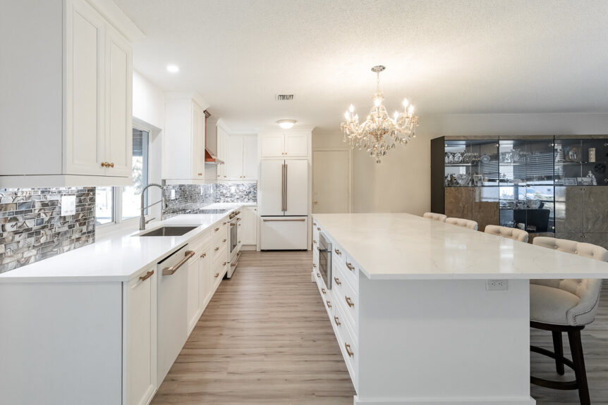 White kitchen with long island, mosaic backsplash and crystal chandelier