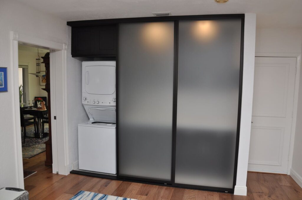 Stacked washer dryer behind sliding frosted door.