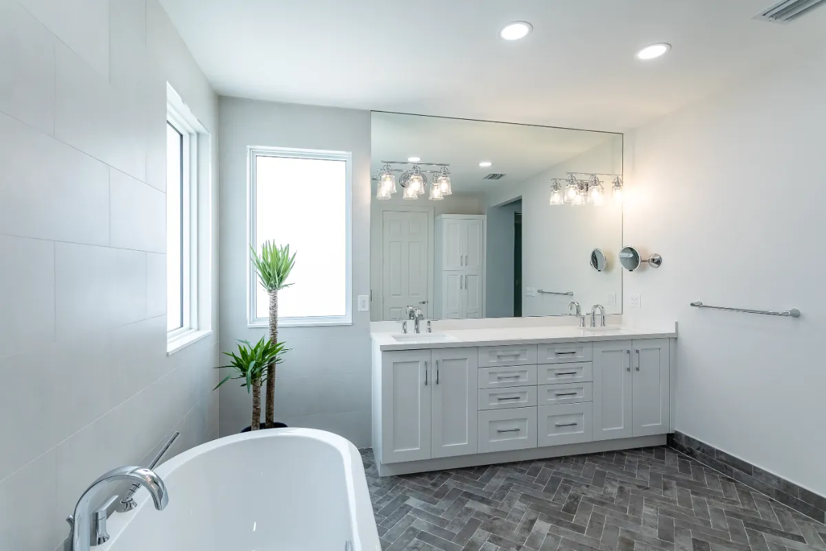 White bathroom with freestanding tub, double vanity and herringbone tile floor