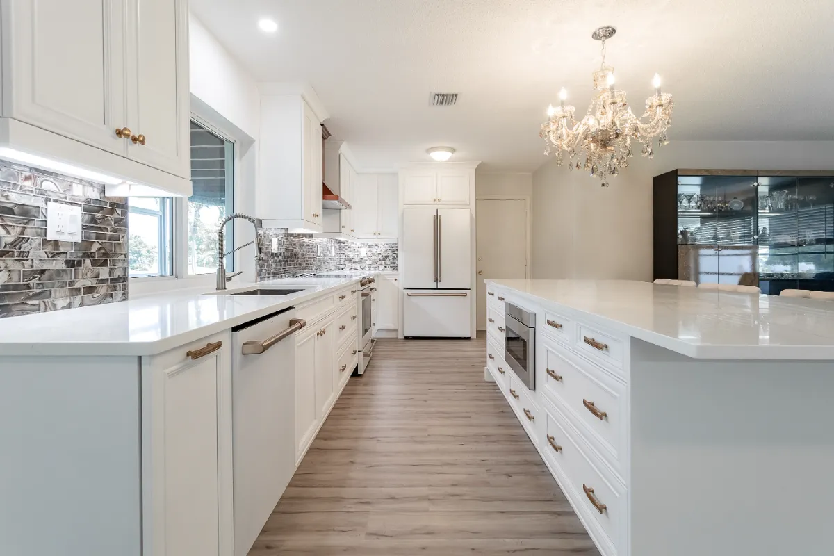 White galley kitchen with long island, mosaic backsplash and chandelier
