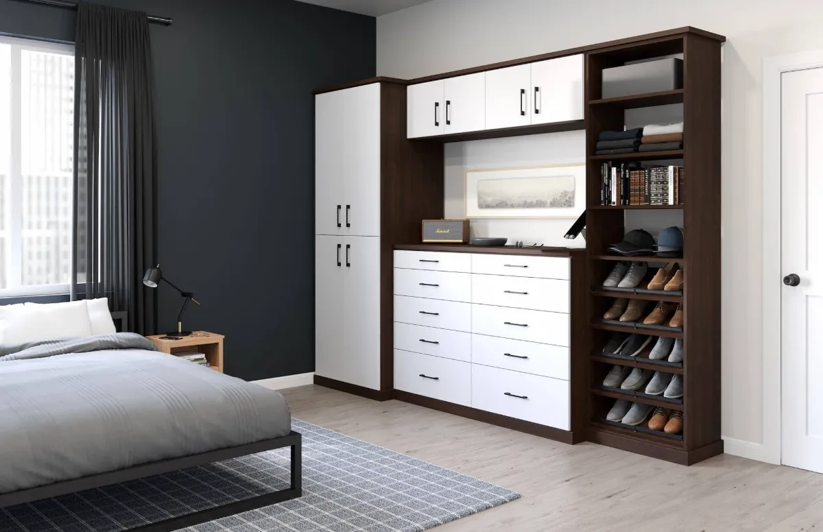 Wall-to-wall bedroom wardrobe with white cabinets, dark wood framing, wide drawers, shelves, and shoe storage